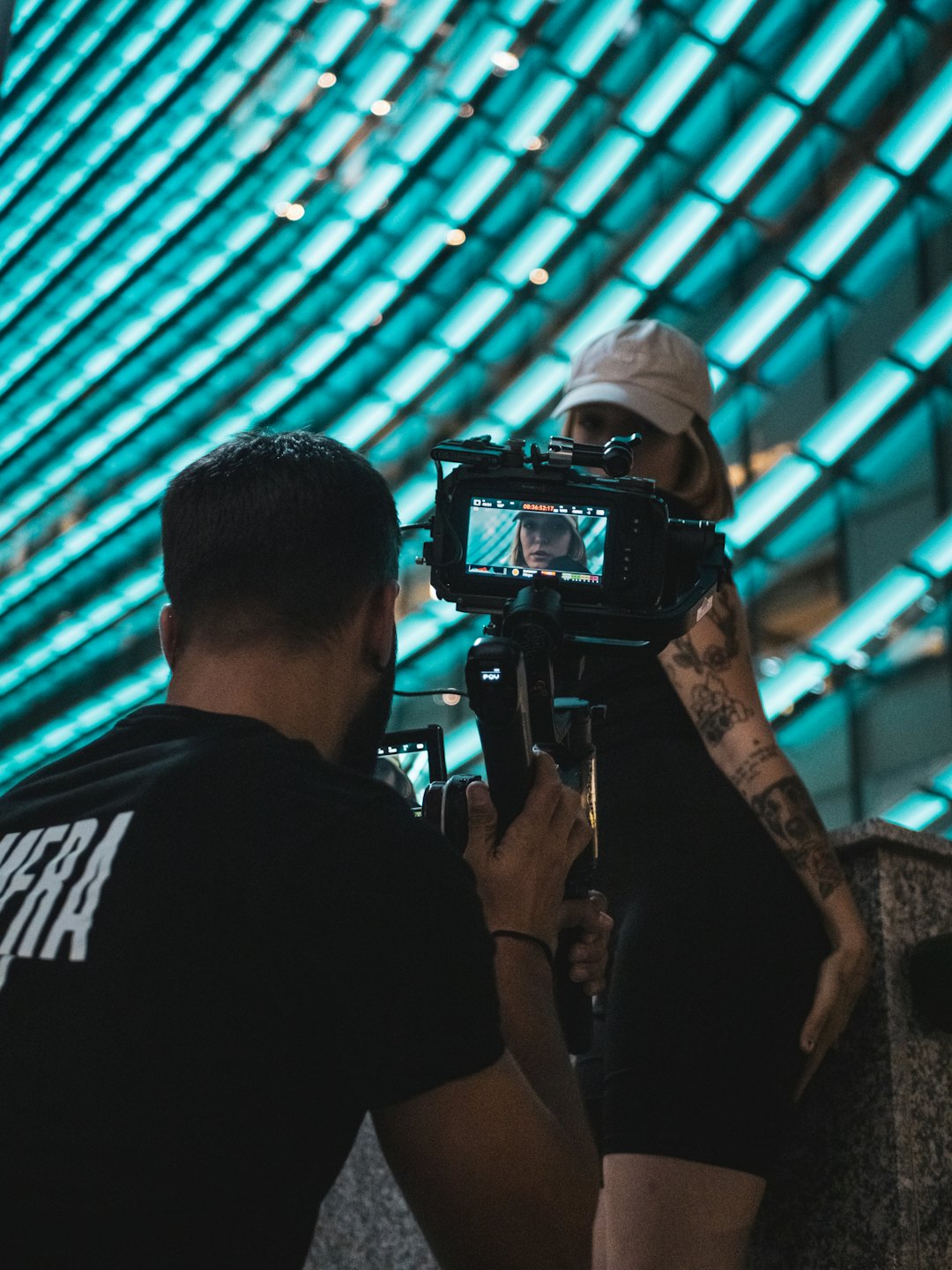 Filmowiec nagrywający kobietę przed nowoczesnym budynkiem.